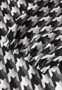 Svart och vit houndstooth-mönstrad tyg med en rynkad kant. Texturen är slät och visar varierande nyanser av grått.
