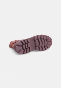 Botín de textil marrón con un acabado texturizado, que presenta una amplia suela de goma morada y rugosa con un dibujo pronunciado para mejorar el agarre.