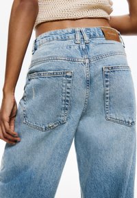 Jasnoniebieskie dżinsy o luźnym kroju, z dwiema tylnymi kieszeniami, widocznym przeszyciem oraz brązową skórzaną metką na pasku.