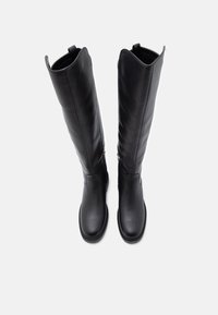 Botas de couro pretas até ao joelho com uma superfície lisa, bico arredondado e detalhe de fecho lateral. O design apresenta uma estética minimalista.