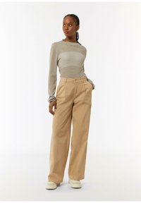 Gestreepte lange mouwen top in beige en donkerbruin, gecombineerd met hoge taille, wijde khaki broek. Casual schoenen maken de look compleet.