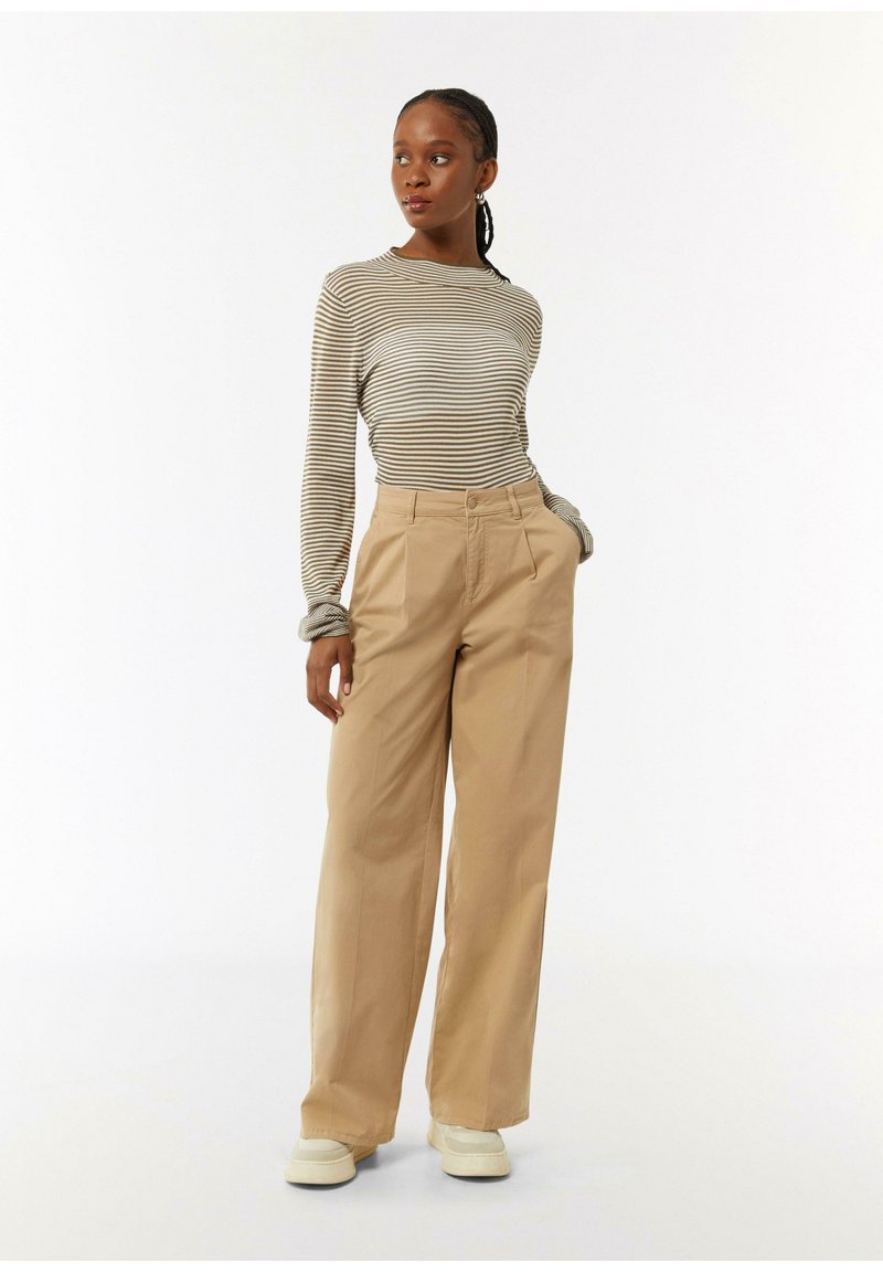 Gestreepte lange mouwen top in beige en donkerbruin, gecombineerd met hoge taille, wijde khaki broek. Casual schoenen maken de look compleet.