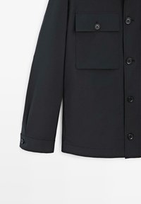 Czarna koszula z długim rękawem, z klapką kieszeni na przodzie, mankietami zapinanymi na guziki oraz pięcioma widocznymi czarnymi guzikami na przodzie.