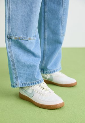 Baskets blanches avec des accents bleu clair, tige en mesh texturé et semelle en caoutchouc beige, accompagnées d'un jean en denim bleu clair ample.