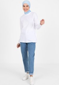 Weißes Langarmshirt kombiniert mit hellblauen Jeans und weißen Sneakers. Das Outfit wird durch ein hellblaues Kopftuch ergänzt und hat eine lockere Passform.