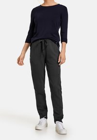 Svarta joggerbyxor med sidofickor, snörning i midjan och en slank design. Kombinerat med en navyblå topp med 3/4-långa ärmar och vita sneakers.