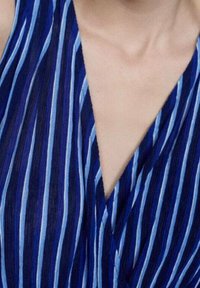 Tissu rayé bleu avec des nuances variées, présentant un design en V. La texture semble légère, avec des rayures verticales fines bien mises en avant.