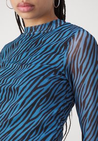 Blå och svart zebramönstrad långärmad topp med hög hals, tillverkad av ett slätt, stretchigt tyg; har genomskinliga ärmar och en figurnära design.