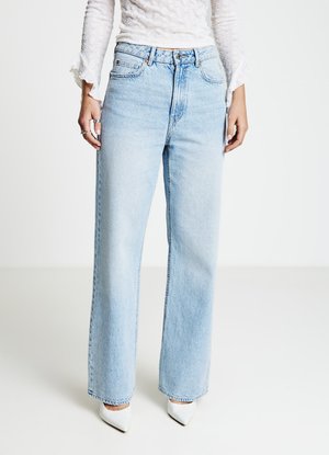 Jeans a gamba larga color azzurro chiaro, in denim, vita alta, design con cinque tasche, abbinati a tacchi bianchi a punta. Leggero effetto usurato visibile.