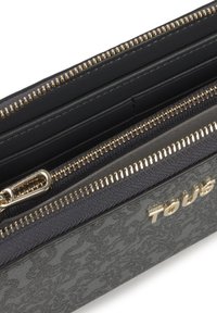 Billetera de cuero negro con herrajes en tono dorado, múltiples compartimentos con cremallera y un patrón texturizado. Nombre de la marca grabado en dorado en el lateral.