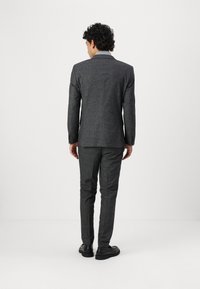Costume carreauté gris au design structuré, avec un col cranté et un pantalon slim-fit, associé à des chaussures noires.