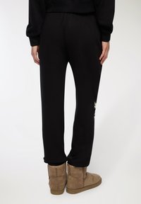 Czarne dresy z elastycznym pasem, zwężanym krojem i detalem z logo na dolnej części nogawki, połączone z beżowymi zamszowymi botkami za kostkę.