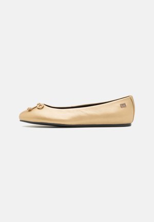 Beige læder balletsko med en lille knude sløjfe på tåen og en sort sål, vist fra siden på en hvid baggrund.