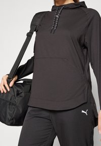 Svart hoodie med dragsko, som har en känguruficka och sidoflikar, tillsammans med svarta byxor som har en liten vit logotyp.