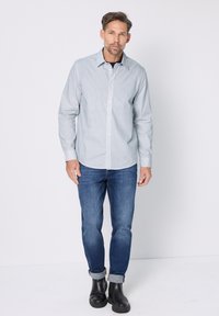 Overhemd met knopen in lichtblauw-wit geruit patroon, gecombineerd met blauwe spijkerbroek en zwarte enkellaarsjes. Het overhemd heeft lange mouwen en een kraag.