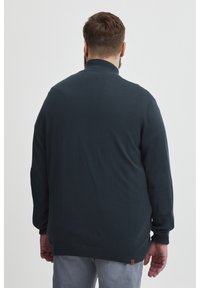 Námořnický svetr s vysokým límcem, žebrovanými manžetami a náplety na loktech. Vyrobený z měkkého materiálu, s mírně texturovaným povrchem.