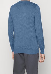 Pull en tricot bleu avec un motif en chevrons, col rond, manches longues et bords côtelés.