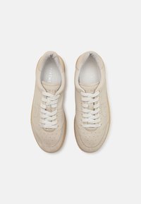Beige lær sneakers med perforerede detaljer, hvide snørebånd og en tan gummisål. Glat tekstur, rund tåform, minimalistisk design.