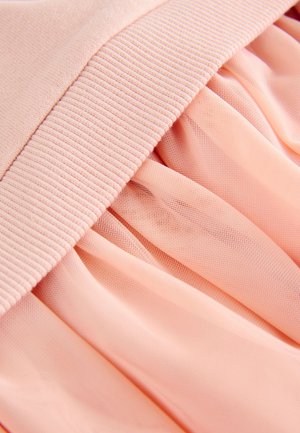 Jasnoróżowy strój z elastycznym, prążkowanym paskiem w talii oraz miękkimi, przezroczystymi plisami z delikatnej tkaniny. Faktura wydaje się gładka i subtelna.