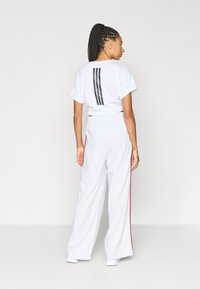 Λευκό κοντό μπλουζάκι με μαύρες κάθετες ρίγες στην πλάτη, συνδυασμένο με ανοιχτό γκρι φαρδιά φόρμα με κόκκινες ρίγες στο πλάι.