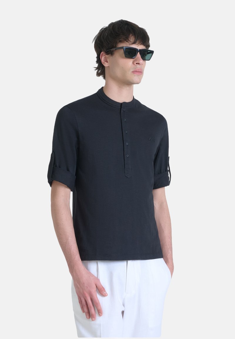 Maglietta henley nera a maniche corte con scollatura curvata e patta bottoni, presenta polsini arrotolati e un logo sottile sul petto.