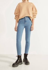 Beige oversize sweatshirt, ljusblå högmidjade skinny jeans och svarta snörda klumpiga stövlar med tjock sula.