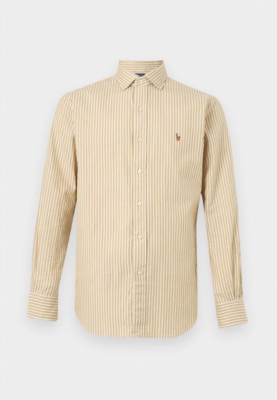 Μπεζ πουκάμισο με μακριά μανίκια, κουμπιά μπροστά, με λευκές κάθετες ρίγες και μικρό κεντητό λογότυπο στο αριστερό στήθος.