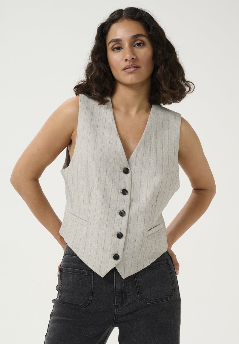 Gilet rayé gris avec un décolleté en V profond, cinq boutons noirs et deux poches avant. Porté sur un pantalon en denim foncé, mettant en valeur une coupe ajustée.
