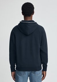 Sudadera con capucha de color azul marino oscuro, con cordón ajustable en la capucha, puños y bajo acanalados. Tela suave, diseño sencillo y detalles mínimos de costura.