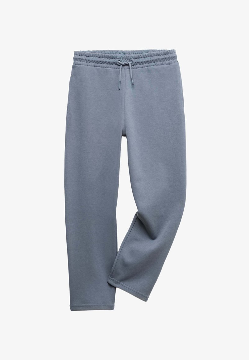 Hellblaue Jogginghose mit elastischem Bund und Kordelzug, ein Bein über das andere geschlagen, auf weißem Hintergrund dargestellt.