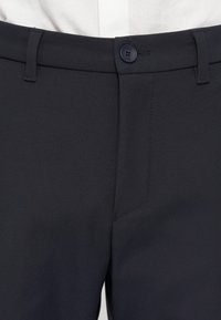 Pantaloni navy confecționați dintr-un material texturat, având un sistem de închidere cu nasture și un buzunar frontal pe partea dreaptă.