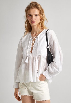 Blusa bianca con ricami floreali, scollatura rotonda e chiusura a stringa. Presenta un corpetto arricciato e maniche lunghe con polsini scallop.