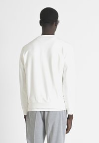 Sudadera blanca de manga larga con cuello redondeado, puños y dobladillo acanalados, hecha de tejido suave, exhibida contra un fondo blanco.