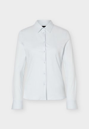 Camicia bianca a maniche lunghe con bottoni, colletto appuntito e silhouette aderente, mostrata su uno sfondo chiaro e semplice.