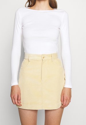Witte lange mouwen top gecombineerd met een lichtgele corduroy minirok met een ceintuur in de taille en voorzakken. Gladde textuur en op maat gemaakt pasvorm.