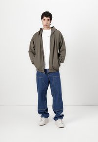 Hooded gray sweatshirt, white crew-neck t-shirt, wide blue denim pants with visible stitching, and white sneakers.
