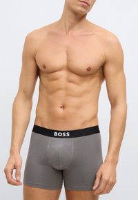Γκρι boxer briefs κατασκευασμένα από απαλό ύφασμα, με μαύρη μέση που φέρει το λογότυπο "BOSS". Το σχέδιο είναι εφαρμοστό και έχει ομαλή υφή.