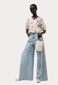 Blusa floreale leggera e trasparente con maniche a palloncino, abbinata a jeans in denim blu a vita alta e gamba larga. Tieni una borsa di perline bianca.