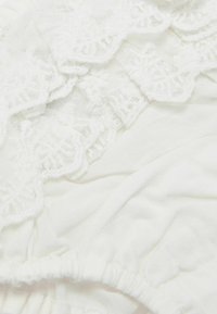 Weißer Stoff mit Spitzenbesatz und gewelltem Rand, weiche Textur und gerafftem Taillendetail, das ein zartes Erscheinungsbild verleiht.