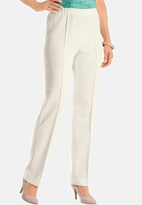 Un pantalon blanc côtelé avec une taille élastique à enfiler et deux coutures verticales à l'avant, associé à des chaussures à talons hauts roses pâles.