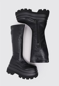 Botas de cuero negro hasta la rodilla con una suela de plataforma gruesa, que cuentan con un cierre lateral y una textura suave. Color sólido sin patrones visibles.