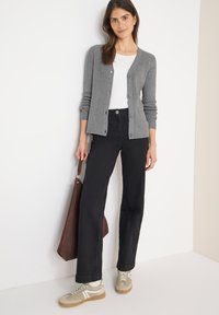 Szary prążkowany kardigan, biała koszulka, czarne jeansy z szerokimi nogawkami oraz jasne sneakersy. Brązowa torba trzymana z boku; gładkie faktury i dopasowany fason.