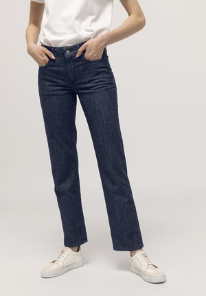 Jeans en denim foncé avec une coupe droite, dotés d'une fermeture à bouton, de poches latérales et d'une texture lisse. Associés à des baskets de couleur claire.