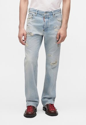 Jean bleu clair délavé porté par une personne, associé à des bottes marron foncé avec des lacets rouges et un haut blanc visible à la taille.