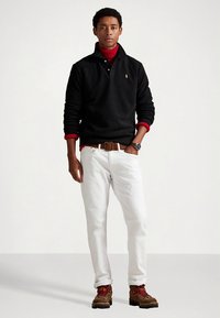 Svart poloskjorte med rød krage, hvite jeans, brunt belte og støvler med røde detaljer. Modell står mot en ensfarget bakgrunn.