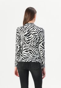 T-shirt à manches longues avec un motif zèbre noir et blanc, en tissu lisse, et un col montant, associé à un jean noir.