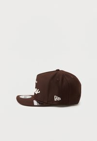 Brown fabric snapback cap featuring white embroidered text and logo accents. Curved visor, structured design, and vent holes on the crown.