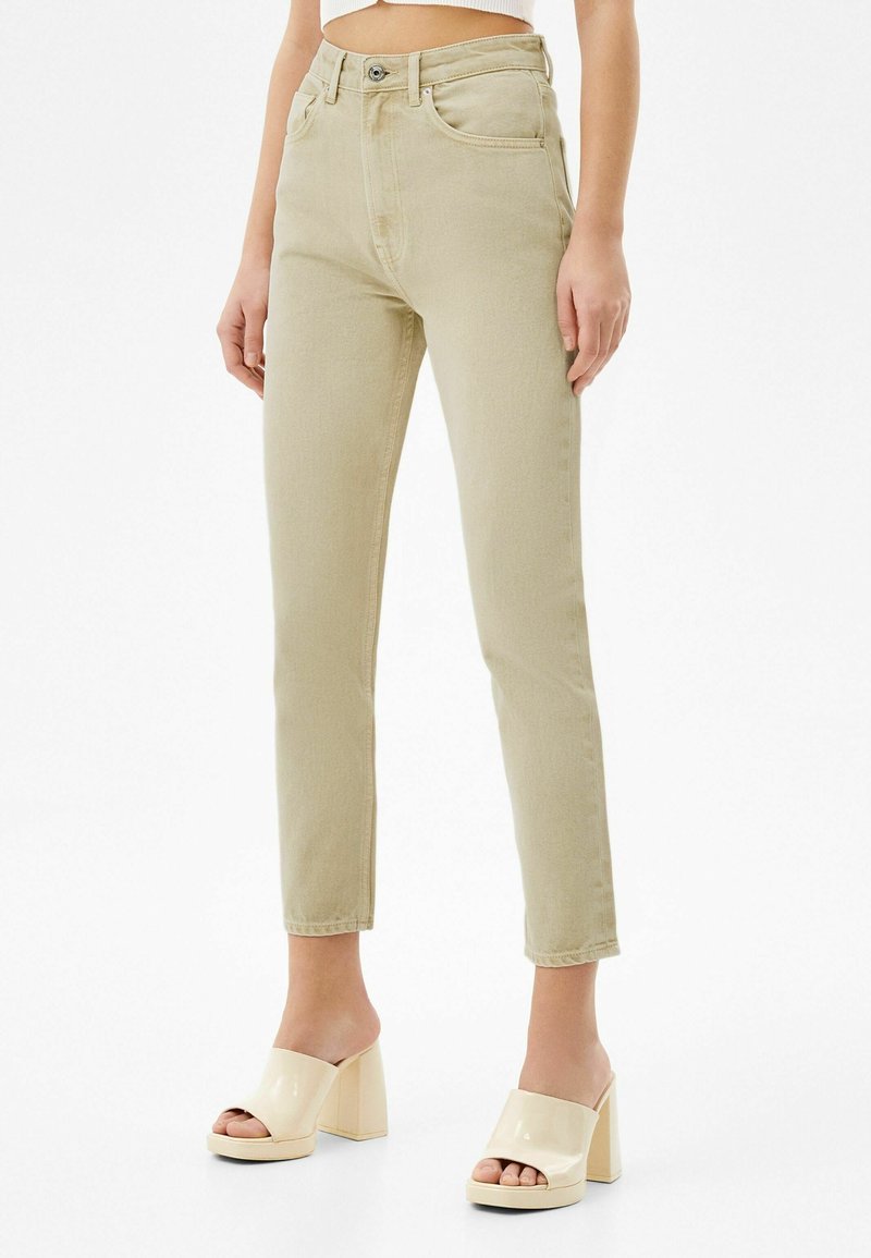 Beiga högmidjade jeans med smal passform, fem fickor och knäppning. Matchas med glänsande beiga klacksandaler med blockklack.