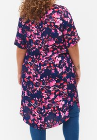 Tunique florale en tissu marine ornée de fleurs roses, à manches courtes, avec un ourlet asymétrique et une texture légère et fluide.