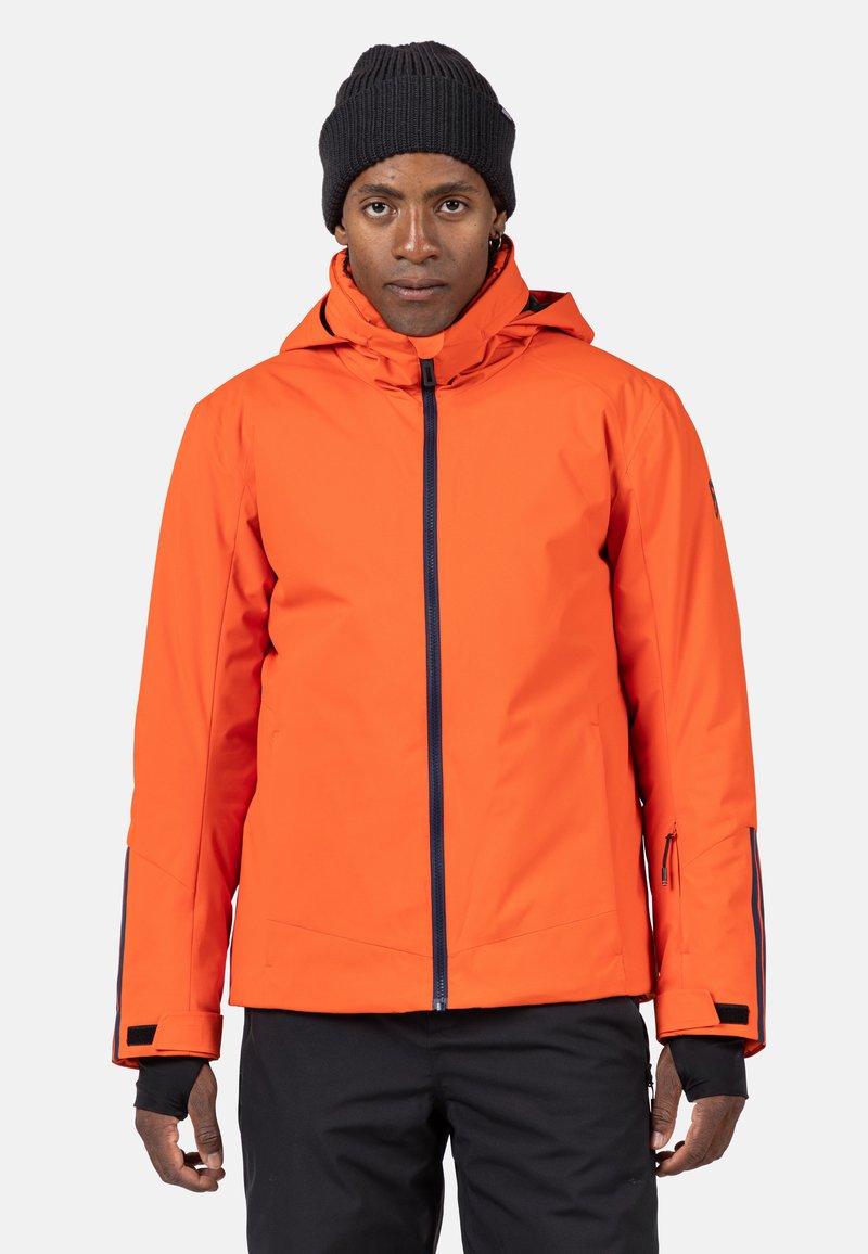 Orange vattentät jacka med huva, med en framdragkedja, dragkedjeförsedda ärmfickor och svarta detaljer.